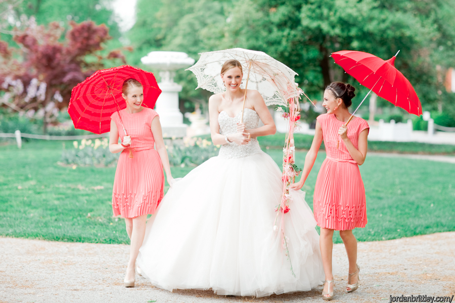 Bride in blush ballgown with her bridesmaids wearing coral and everyone carrying a parasol