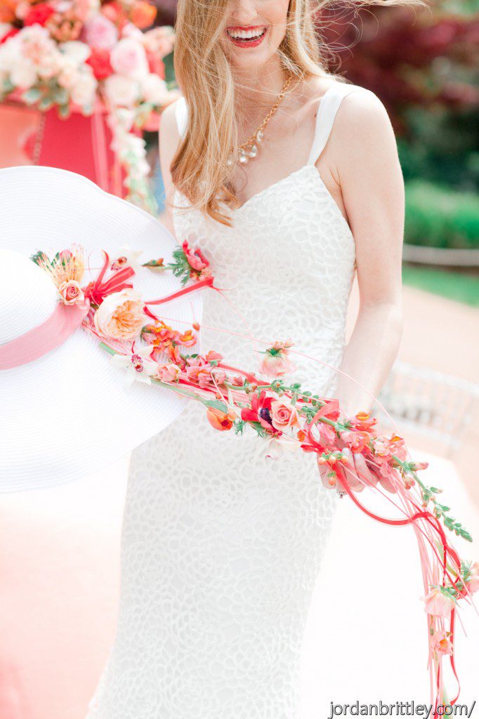smiling bride with red lipstick holding wedding hat with flowers