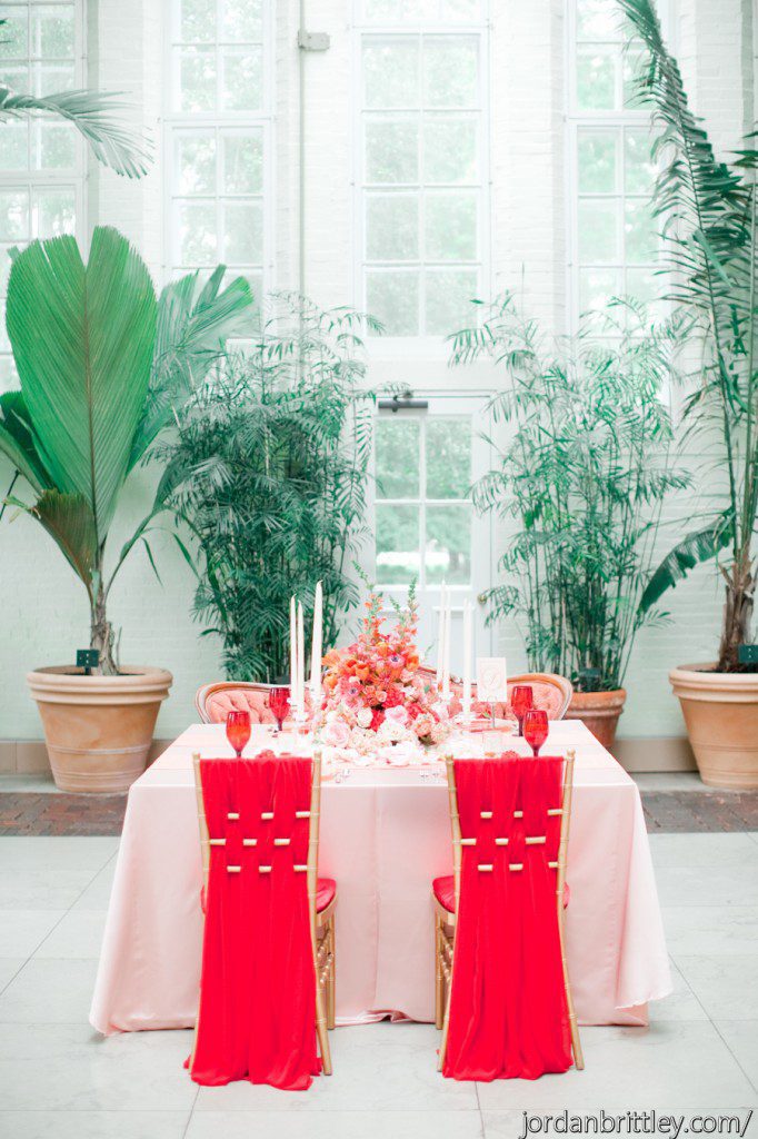 Coral peach table with coral flowers centerpiece and tall candles with red chair fabric chiavaris